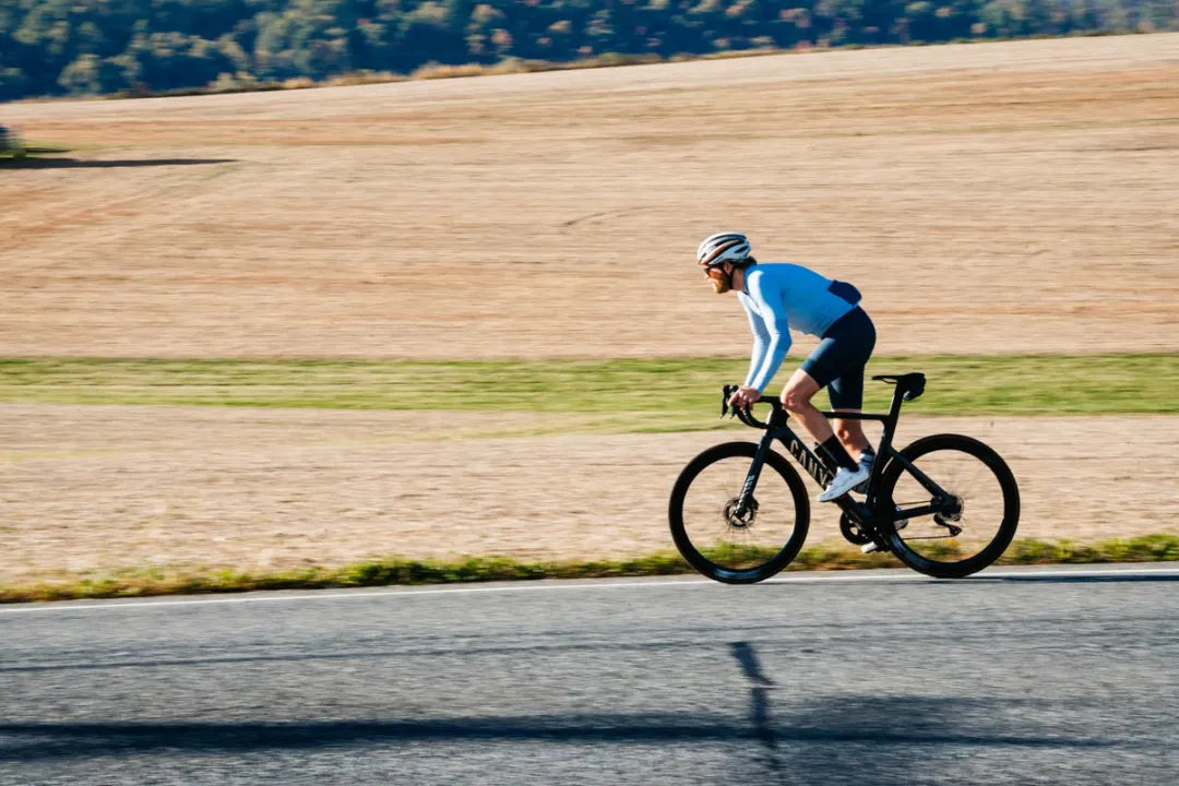 Cyclist riding a Canyon road bike on a flat scenic road, demonstrating steady Zone 2 endurance training.