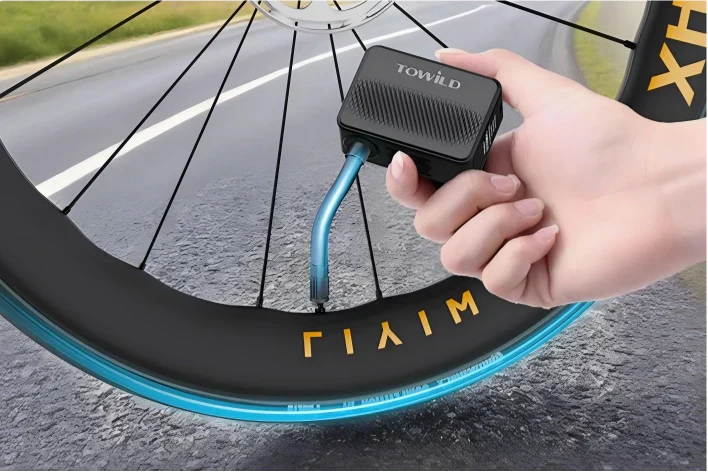 Hand holding the TOWILD A13 Mini Bicycle Tire Inflator to inflate a road bike tire on the roadside.