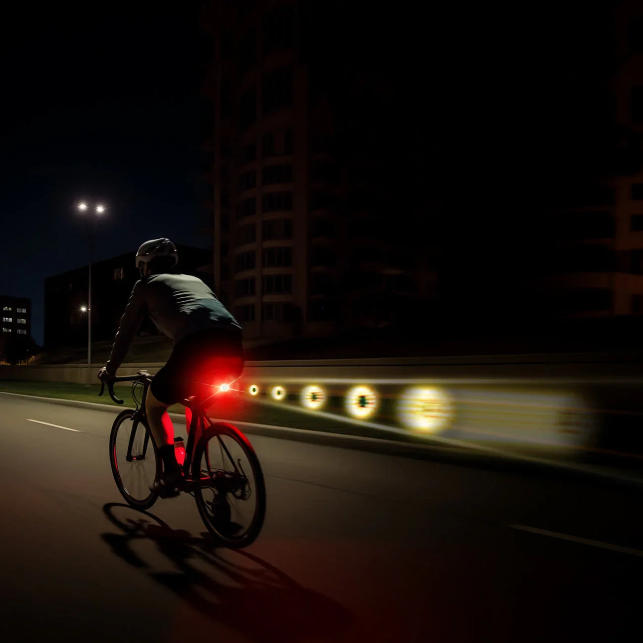 A cyclist riding on a city road at night, with the bright red Towild TL05 rear bike light providing powerful visibility for safety.