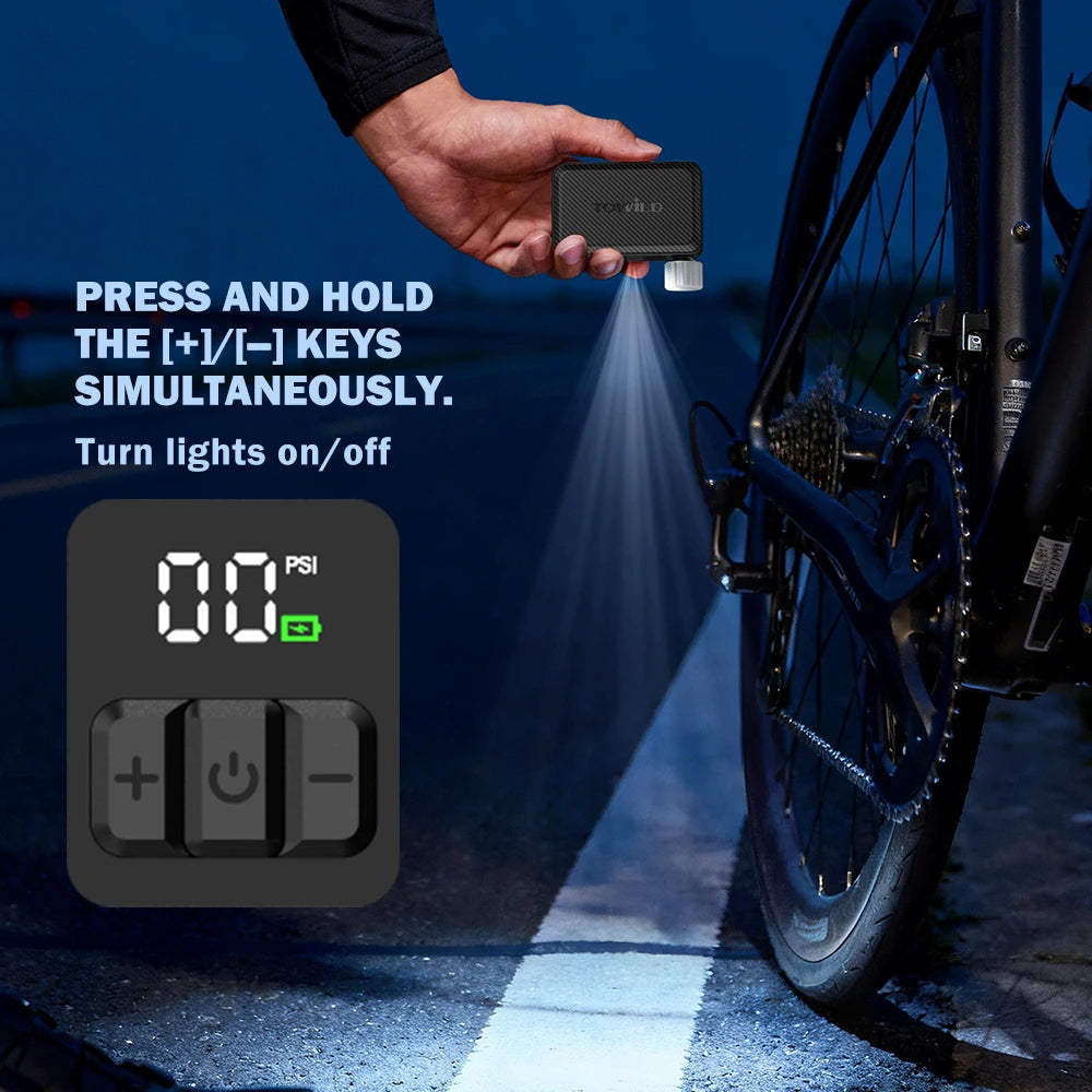 A cyclist using the TOWILD A15 electric bike pump's built-in emergency LED light for a nighttime roadside tire repair. Instructions show: press and hold the +/- keys simultaneously to turn lights on/off.