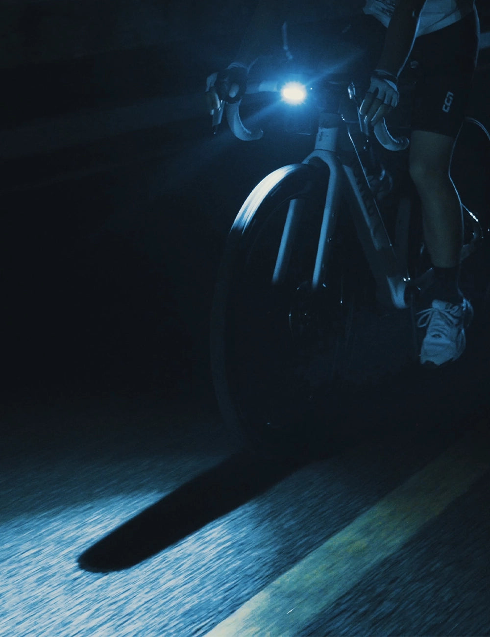A cyclist rides at night with the TOWILD BL1500 front light illuminating the road near the front wheel.