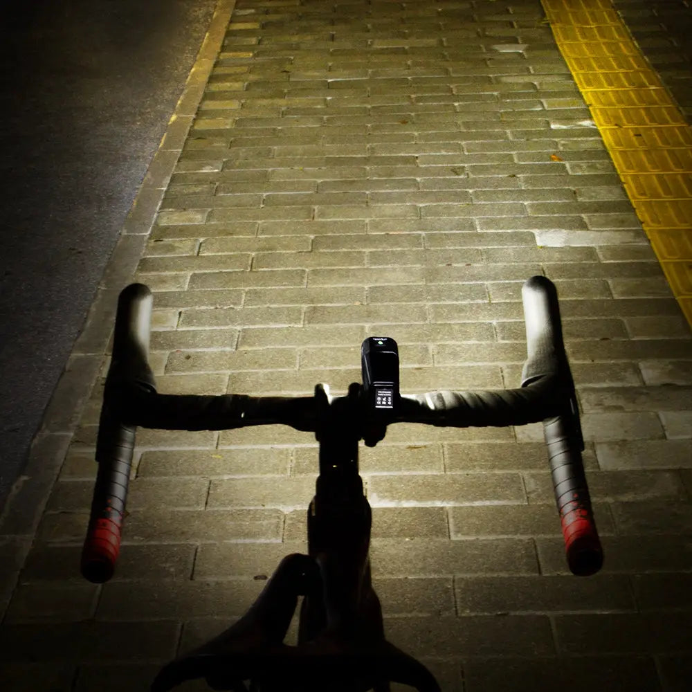 Rider's point-of-view of the Towild BR1000 bike light casting a wide, bright beam on a brick path during a night ride, ensuring clear visibility.